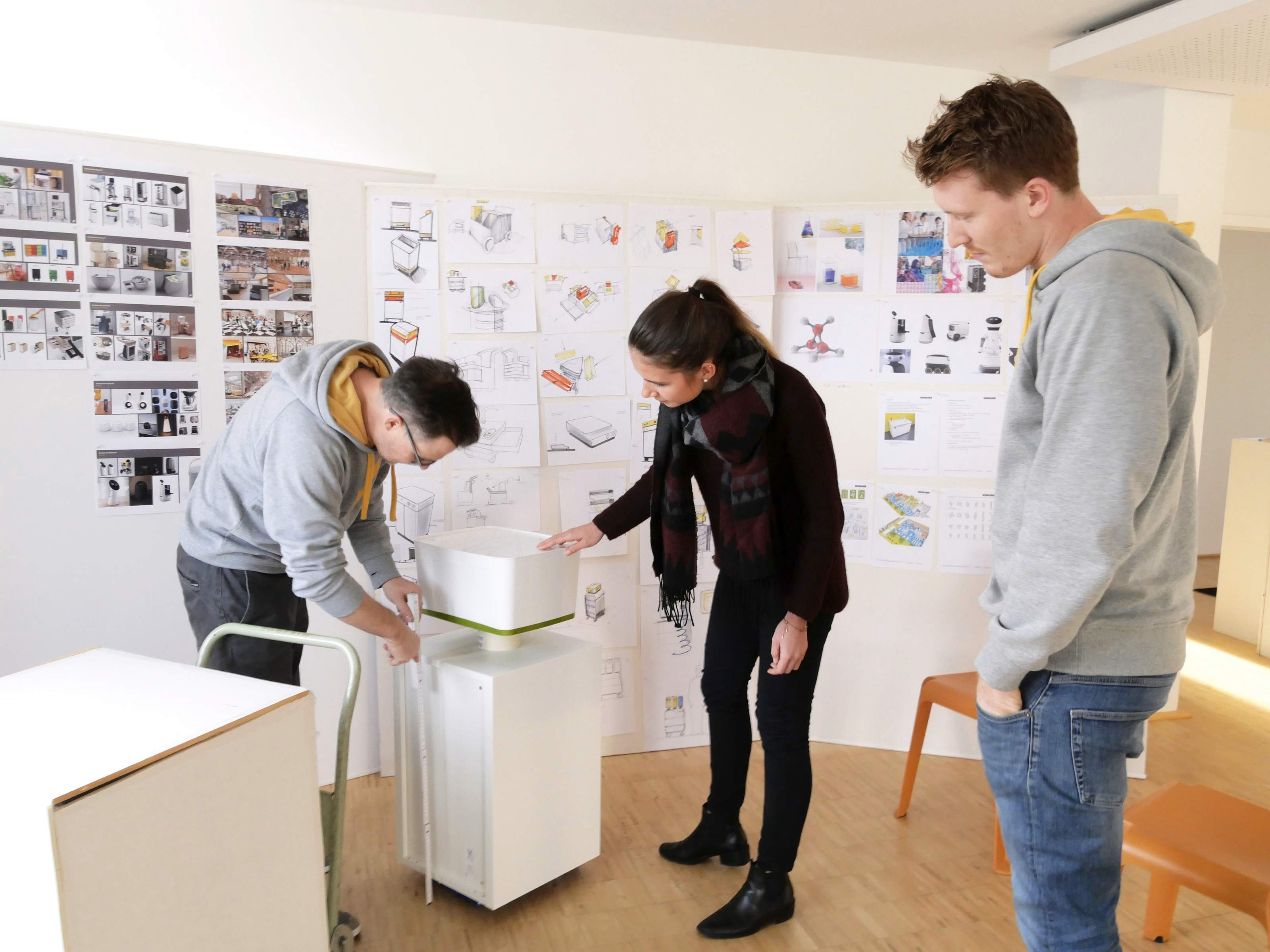 Design team discussing a medienBuddy prototype in front of a wall of sketches