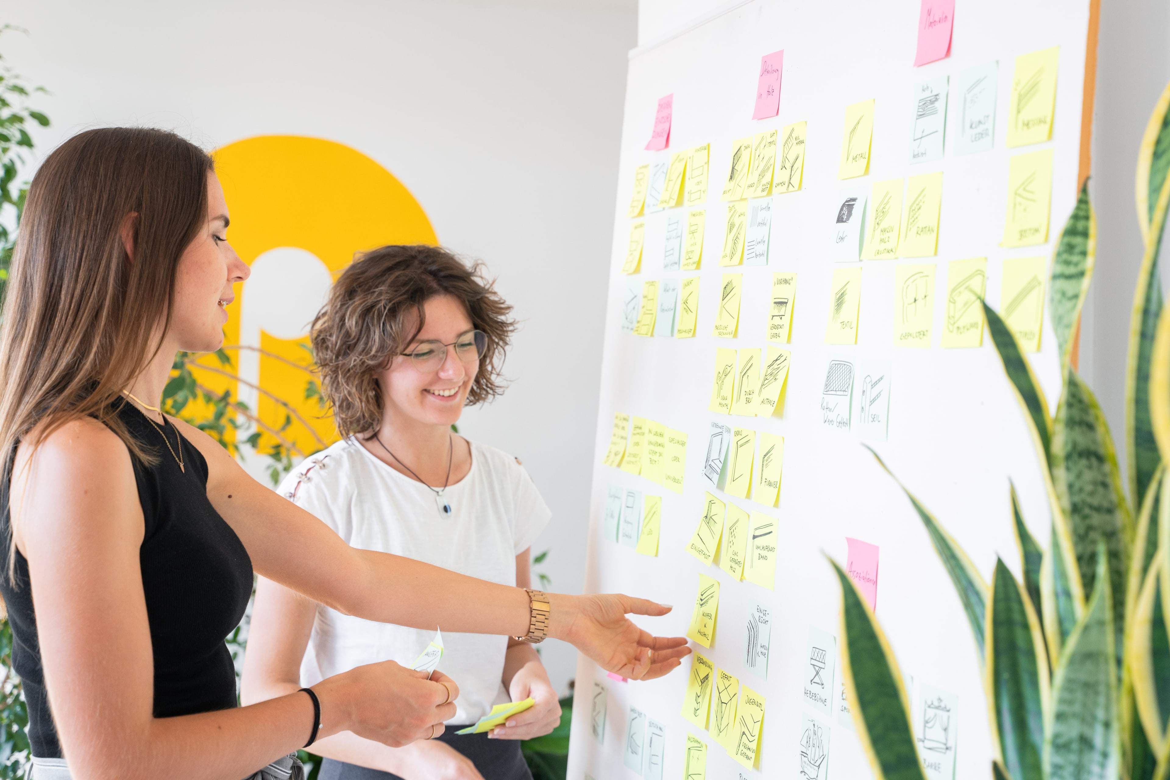 Zwei Frauen ordnen Post-its und Skizzen an einer Workshop-Wand