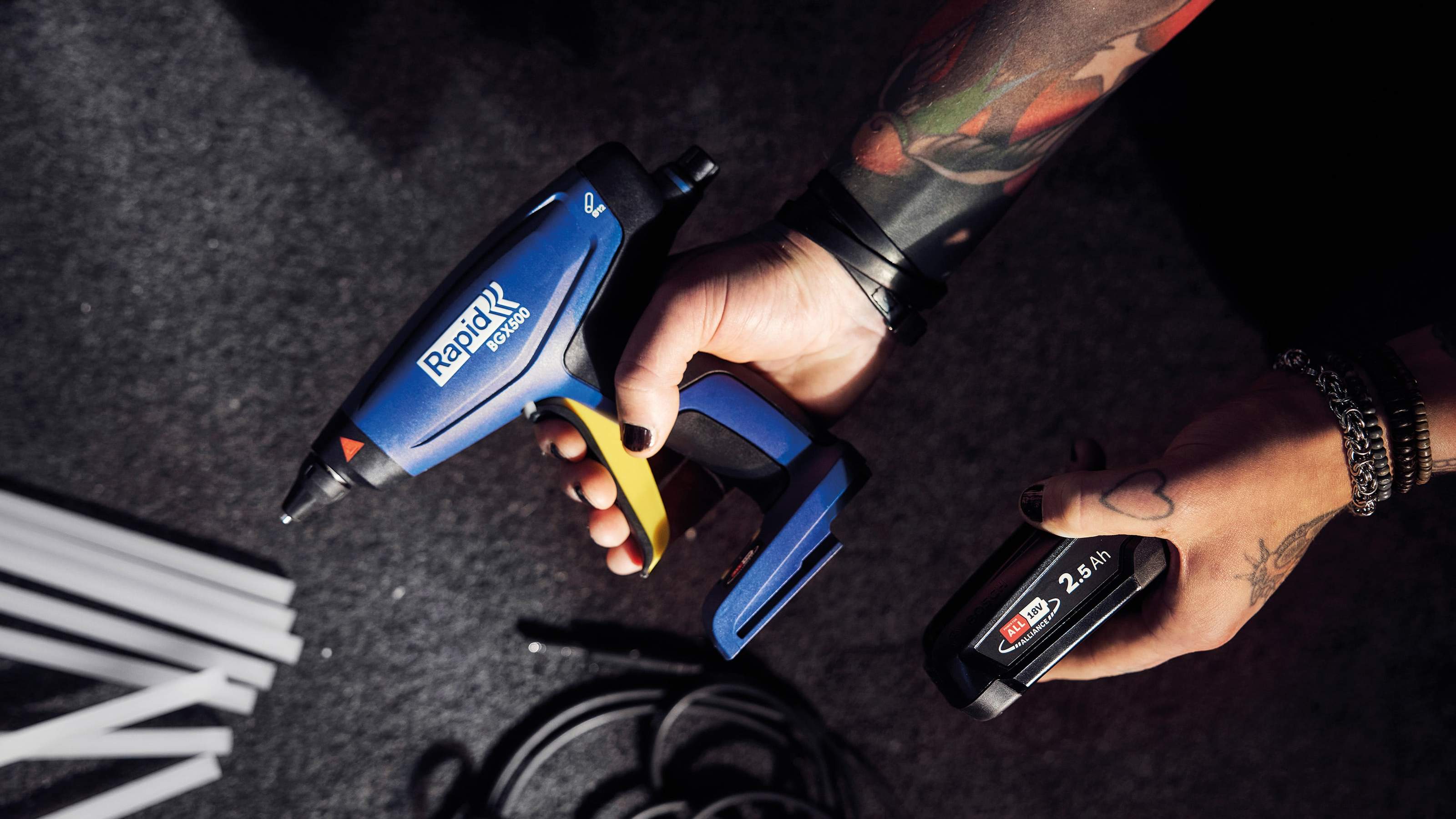 Tattooed hand holding the Rapid RX1000 hot air gun and its battery in a dark setting